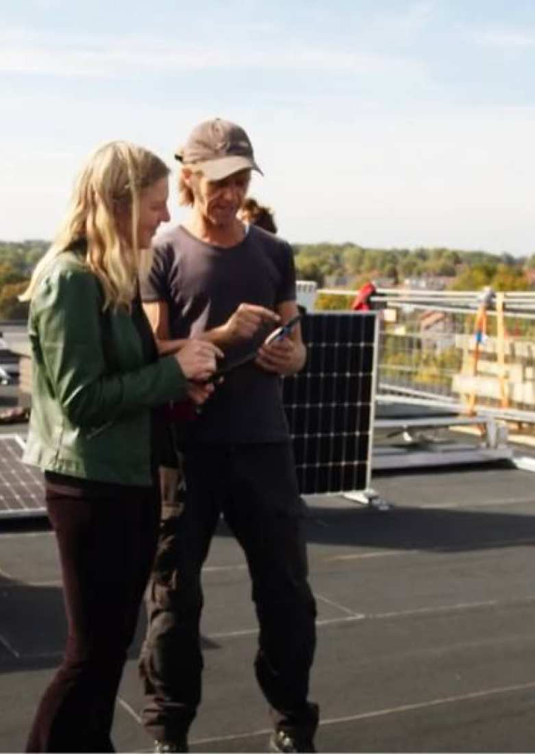 Twee technici overleggen op een dak bij het leggen van zonnepanelen.