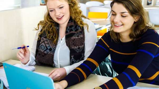 2 vrouwelijke studenten Social Work werken samen op 1 laptop. Ze hebben net hun propedeuse Social Work behaald.