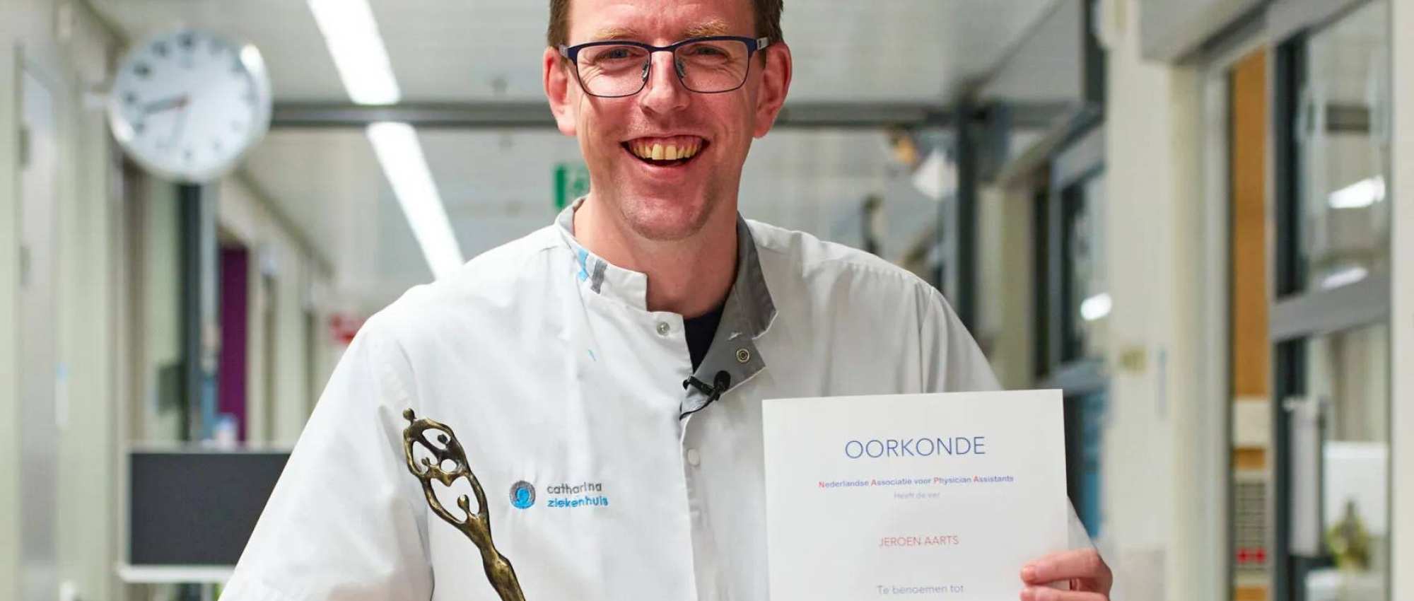 Foto van Jeroen Aarts, verkozen tot PA van het jaar 2022, in doktersjas met oorkonde en beeldje in het Catharinaziekenhuis