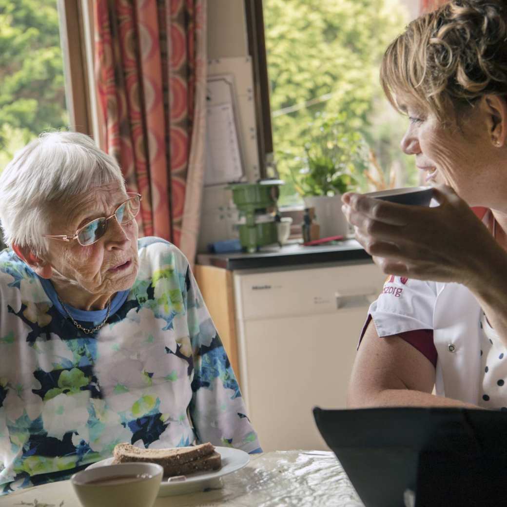 thuiszorgverpleegkundige helpt een nog thuiswonende oudere dame met beginnende dementie bij de dagelijkse zorgtaken