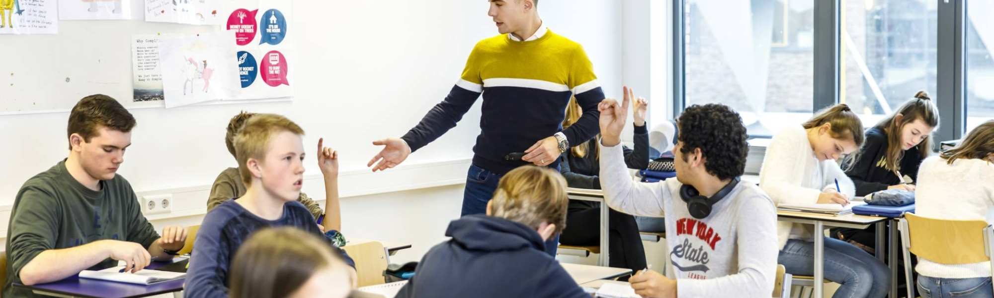 Docent op het Citadel College loopt door het klaslokaal om vragen van de leerlingen te beantwoorden die de vinger in de lucht hebben.