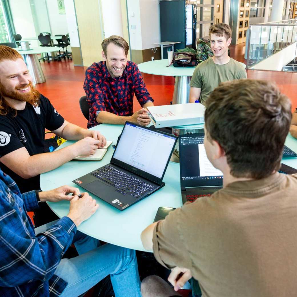 a group of engineering students working on a project together at a round table with laptops 