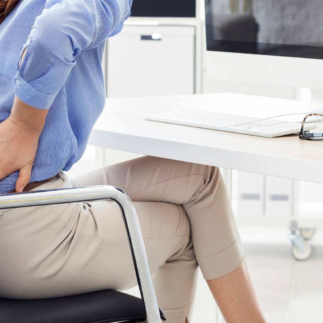 Vrouw achter laptop met lage rugpijn.