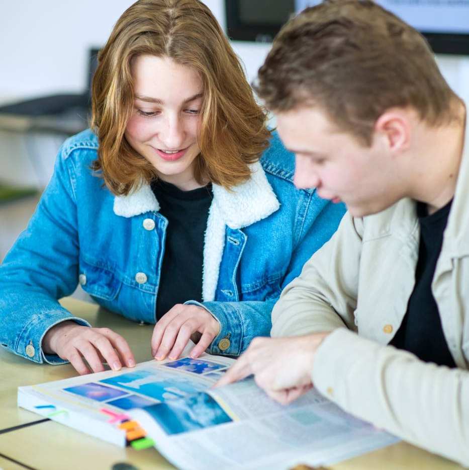 Twee studenten lezen samen in een boek in het lokaal.