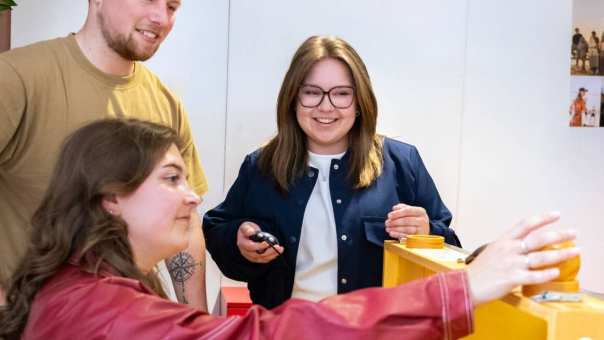 Student demonstreert een hulpmiddel aan 2 medestudenten in het appartement van Ergothetherapie