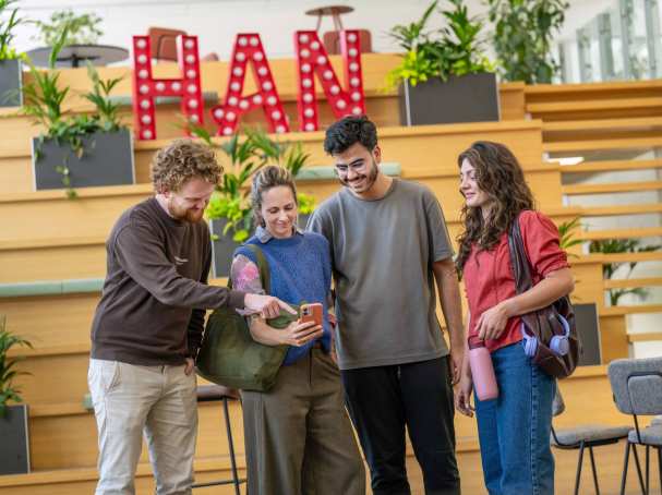 Groep van vier studenten staat in hal en kijken naar telefoon