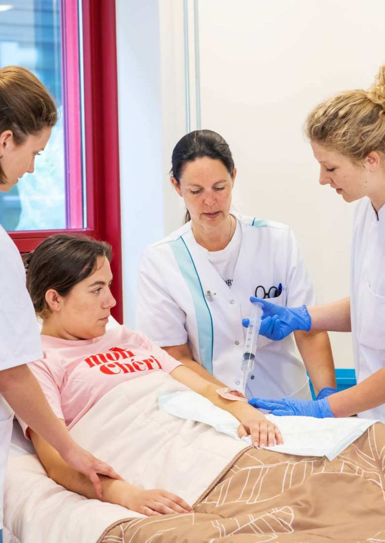 Docent kijkt mee met studenten die bezig zijn met oefenen wondverzorging