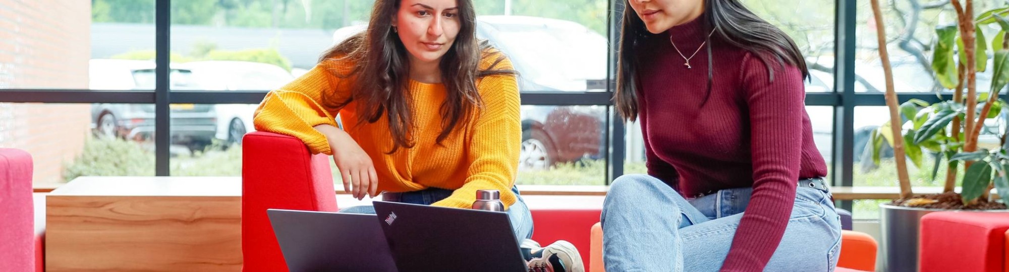 Twee internationael studenten overleggen met laptop bij rode banken