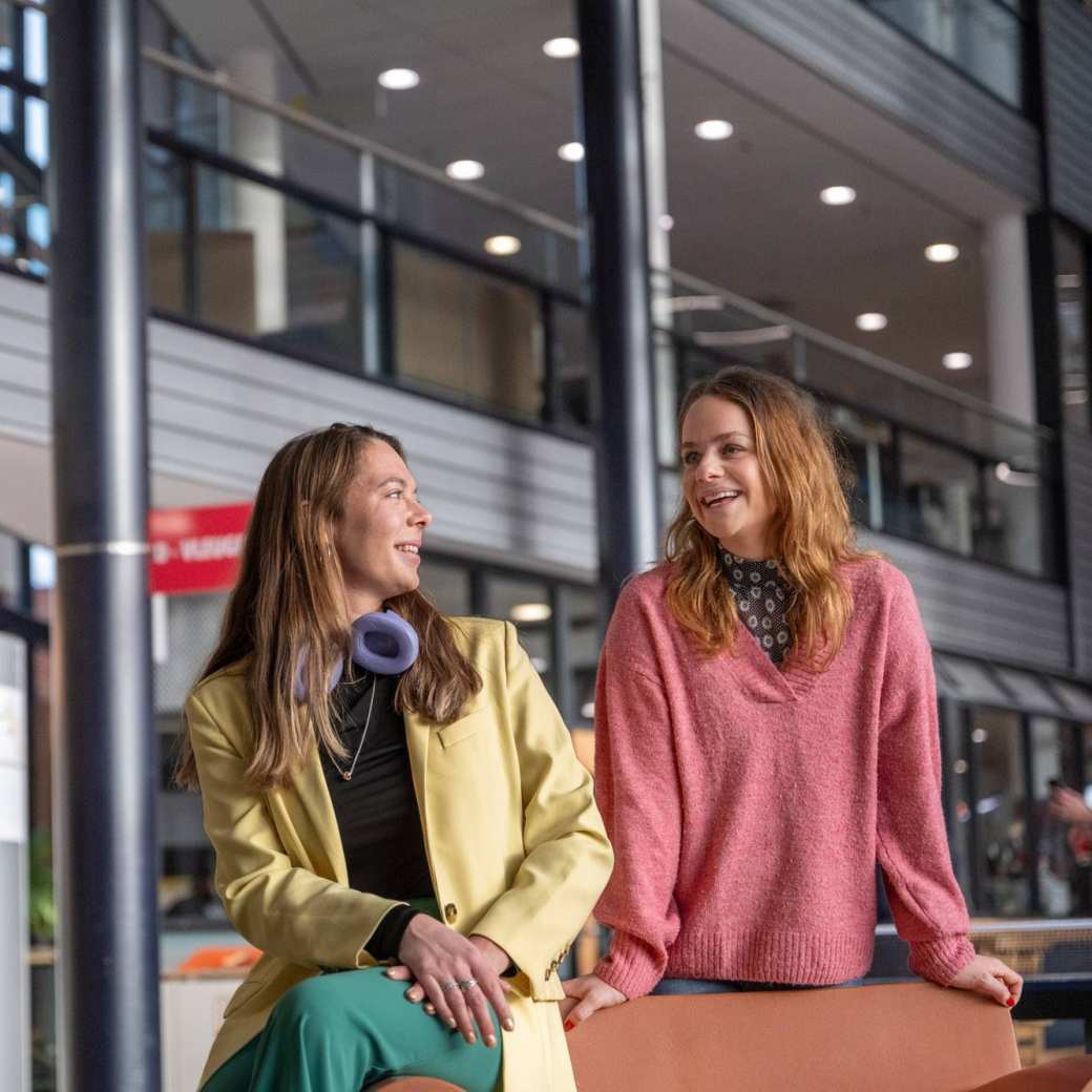 2 studenten staan en zitten in een hal.