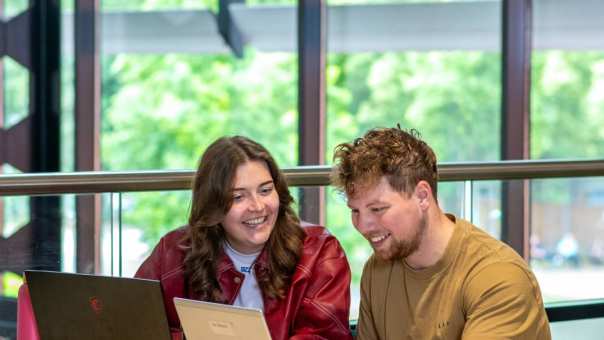 Studenten Ergotherapie zitten aan een tafel met een laptop op de campus in Nijmegen en kijken met elkaar mee
