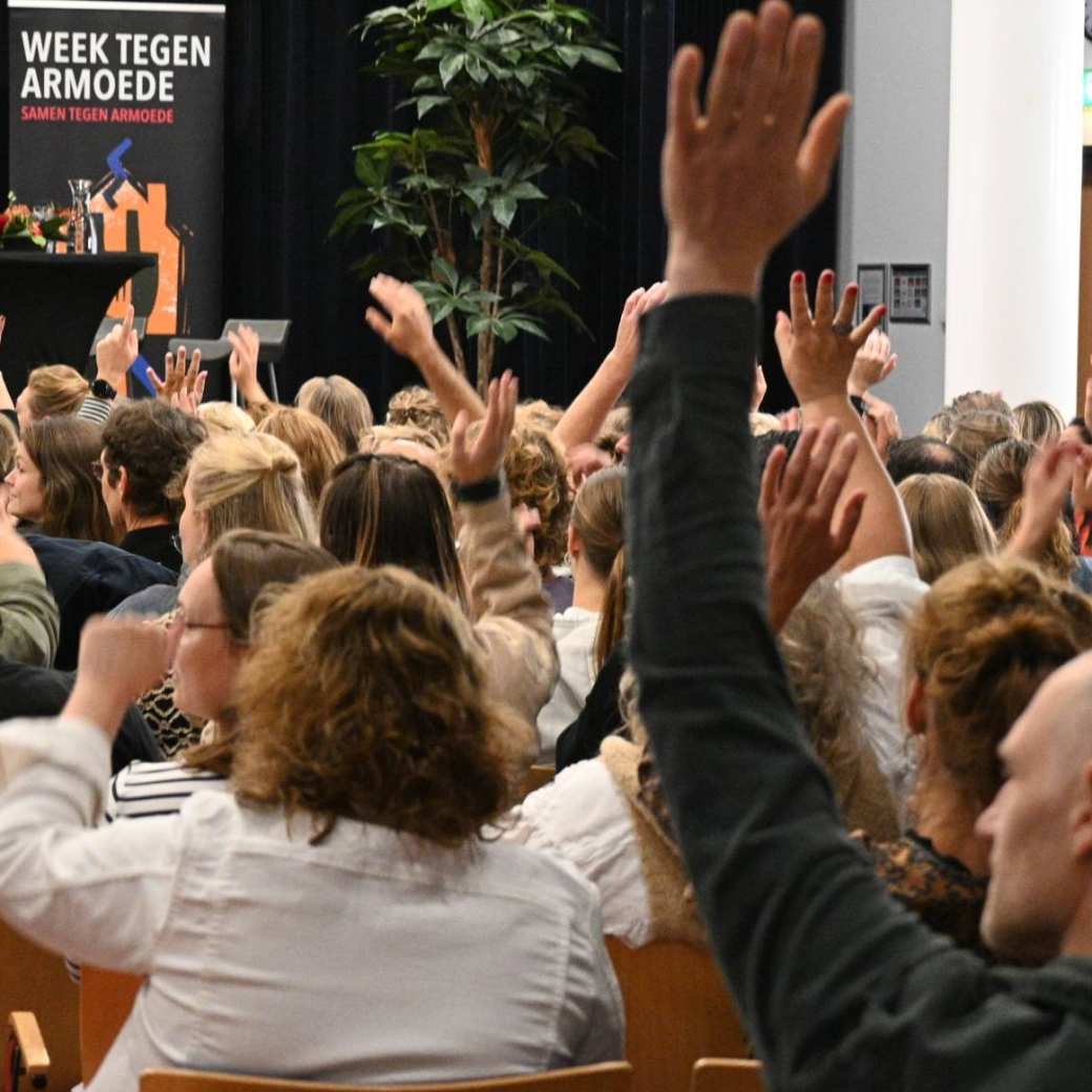 publiek met handen omhoog tijdens symposium beyond borders week tegen armoede