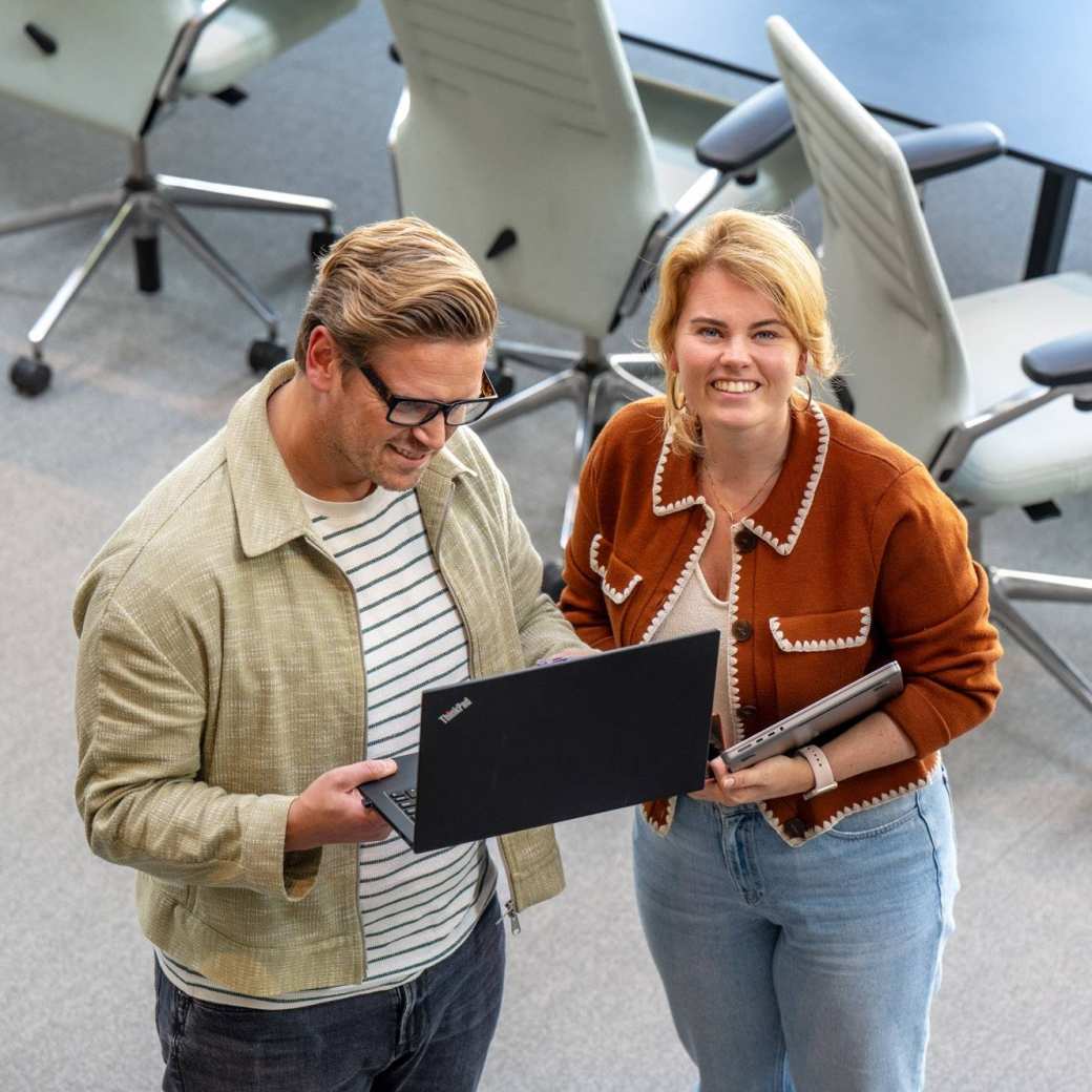 Man en vrouw staan met laptop in de hand en kijken lachend naar camera