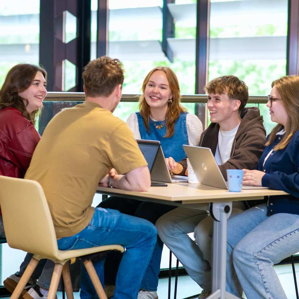 Groep Ergotherapie studenten zitten aan tafel met laptops en overleggen met elkaar.