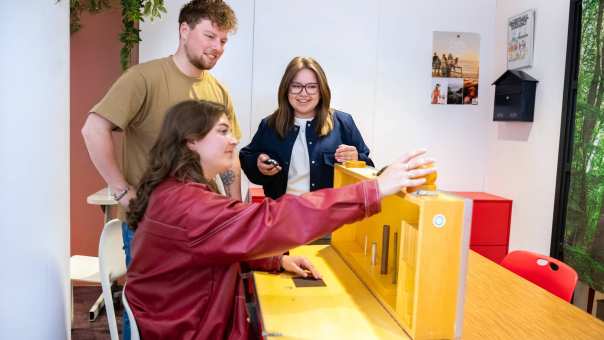 Student demonstreert een hulpmiddel aan 2 medestudenten in het appartement van Ergothetherapie
