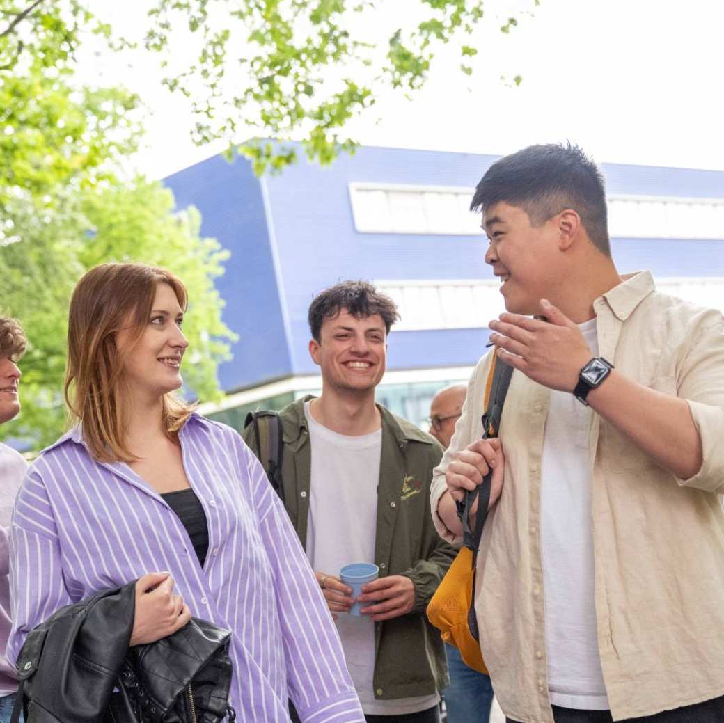 Groepje studenten staan buiten, met elkaar aan het kletsen, op de campus.
