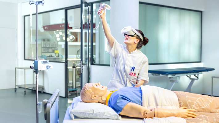 Verpleegkundige oefent met VR bril aan een ziekenhuisbed met dummy.