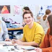 Fotoshoot maakdagen beeldende vorming 2022.Drie studenten met elkaar in overkeg tijdens de les beeldende vorming. De jongen in het midden lacht