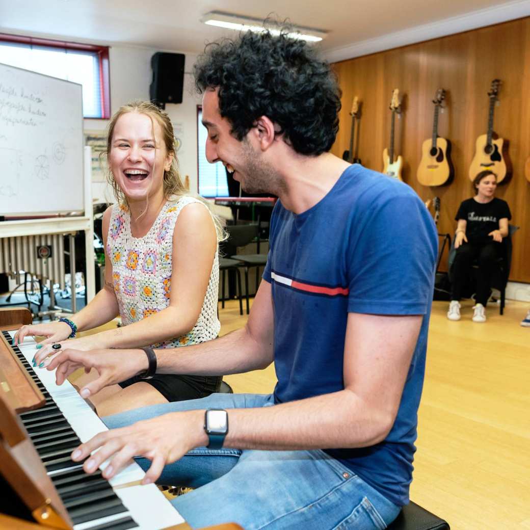 Twee studenten spelen op piano in muzieklokaal