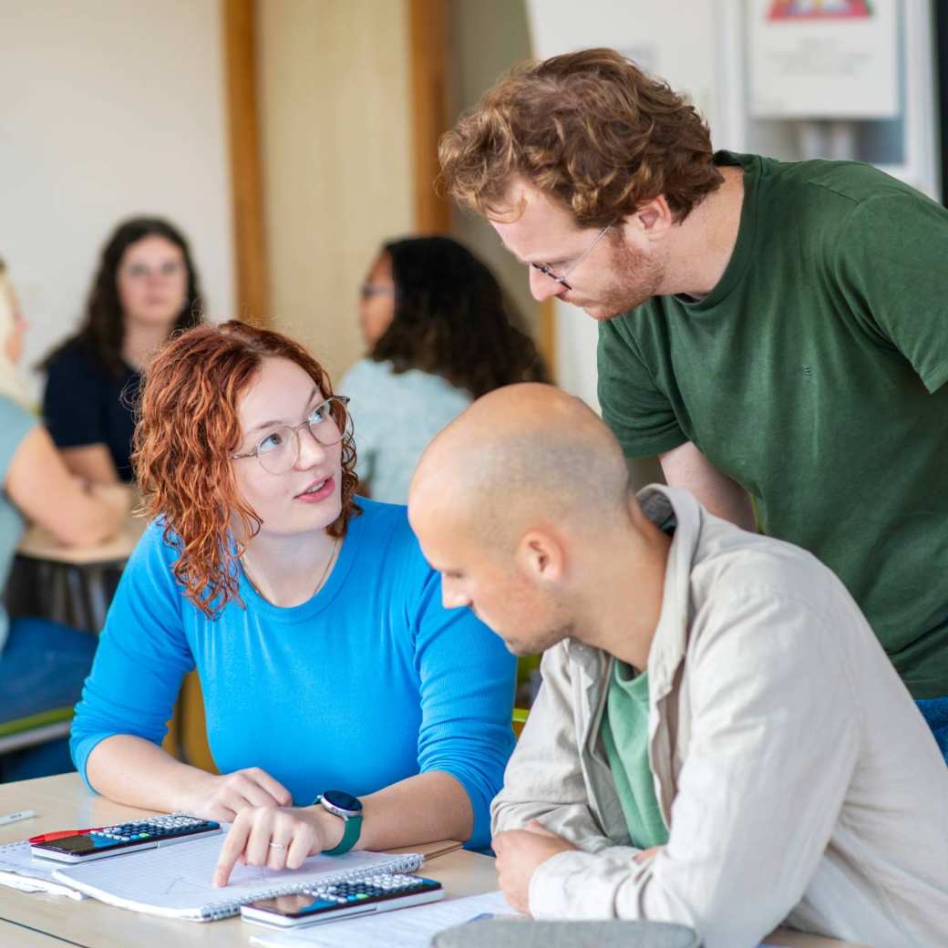 Studenten van Leraar Economie werken aan een groepsopdracht en de docent kijkt toe.