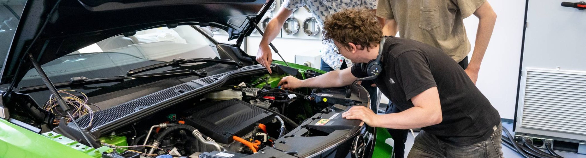 Studenten en docent automotive kijken naar de motor van de auto.