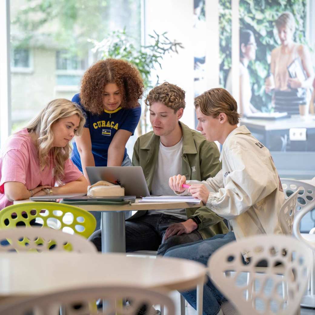 Groepje studenten werken samen aan een ronde tafel in de gang, werkplek in LvS10. Kijken samen naar de laptop.