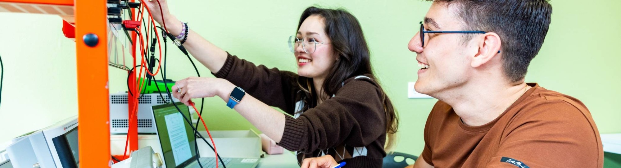 Twee studenten elektrotechniek werken samen aan een logboek tijdens een practicumsituatie.