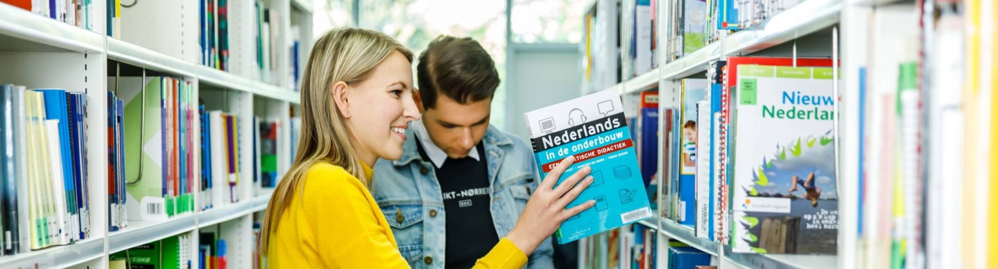 Twee studenten Leraar Nederlanders zijn op zoek naar een boek in de bibliotheek. 