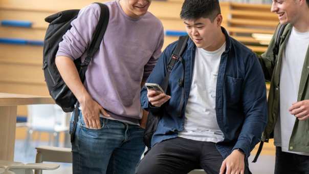 3 studenten/jongens kijken op hun mobiel en lachen