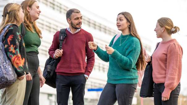 5 studenten praten buiten met elkaar.