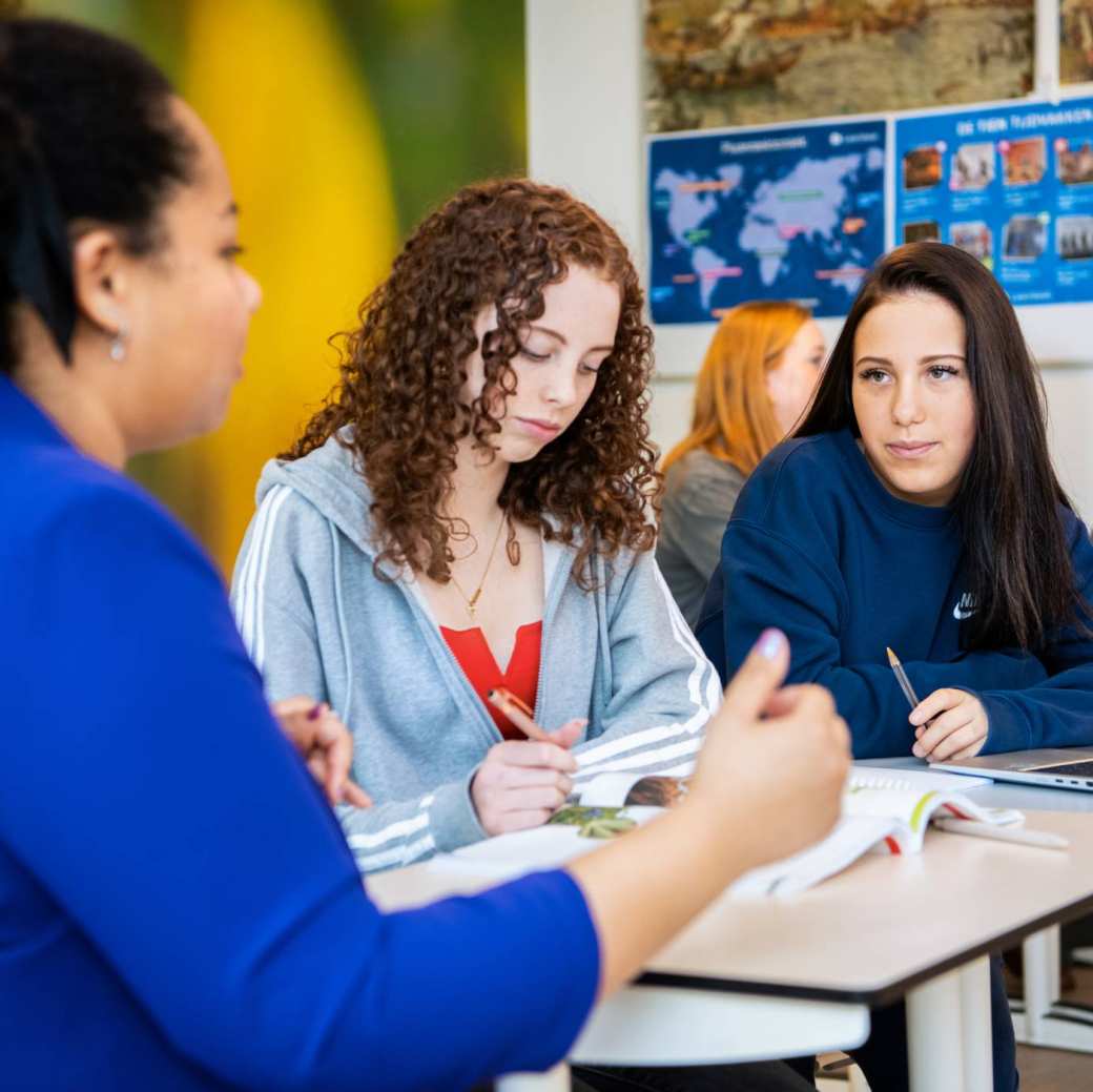 Een student wijst lachend iets aan in de atlas en de andere student kijkt nieuwsgierig toe.