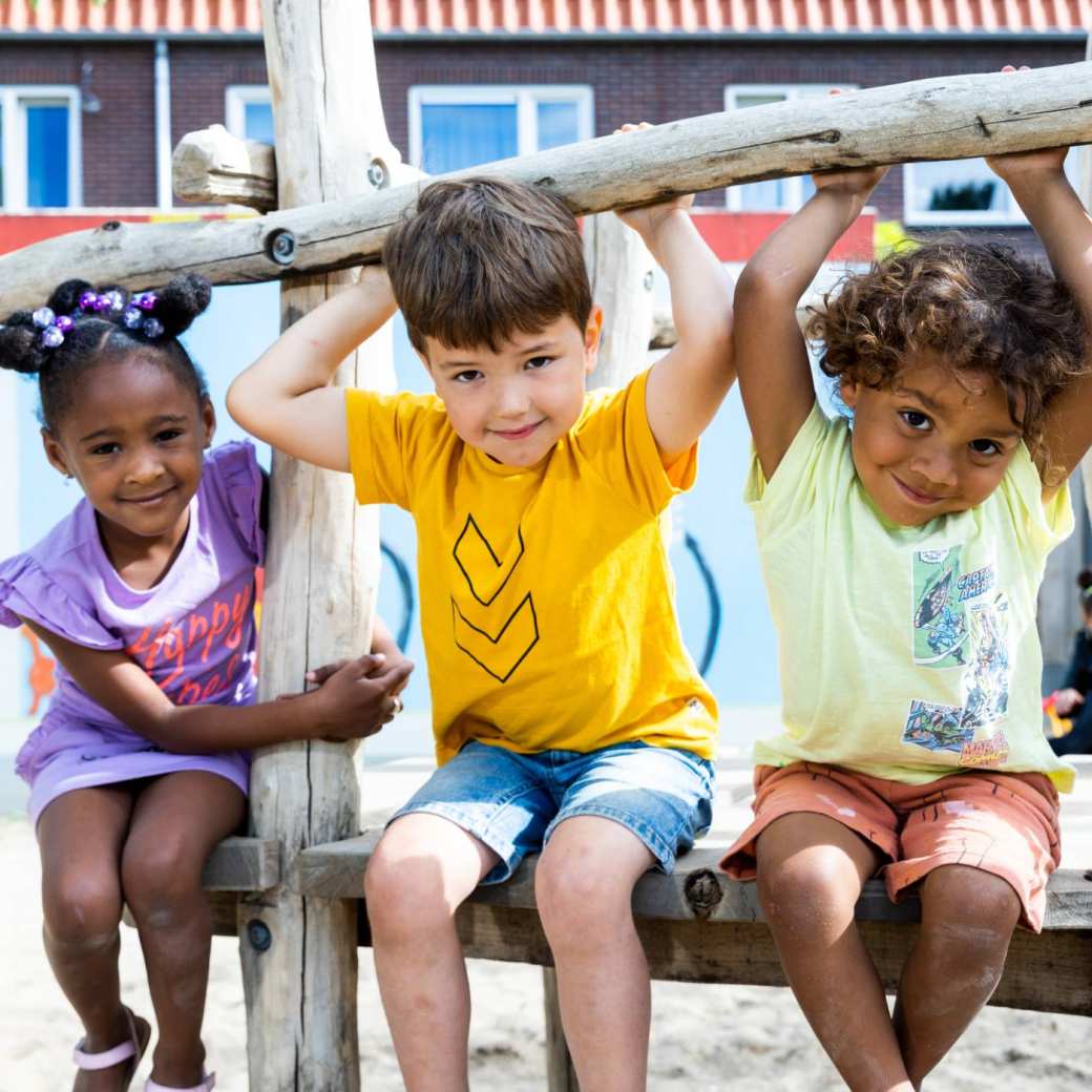 Drie kinderen spelen buiten en hangen aan het klimrek. Foto voor de opleiding leraar basisonderwijs