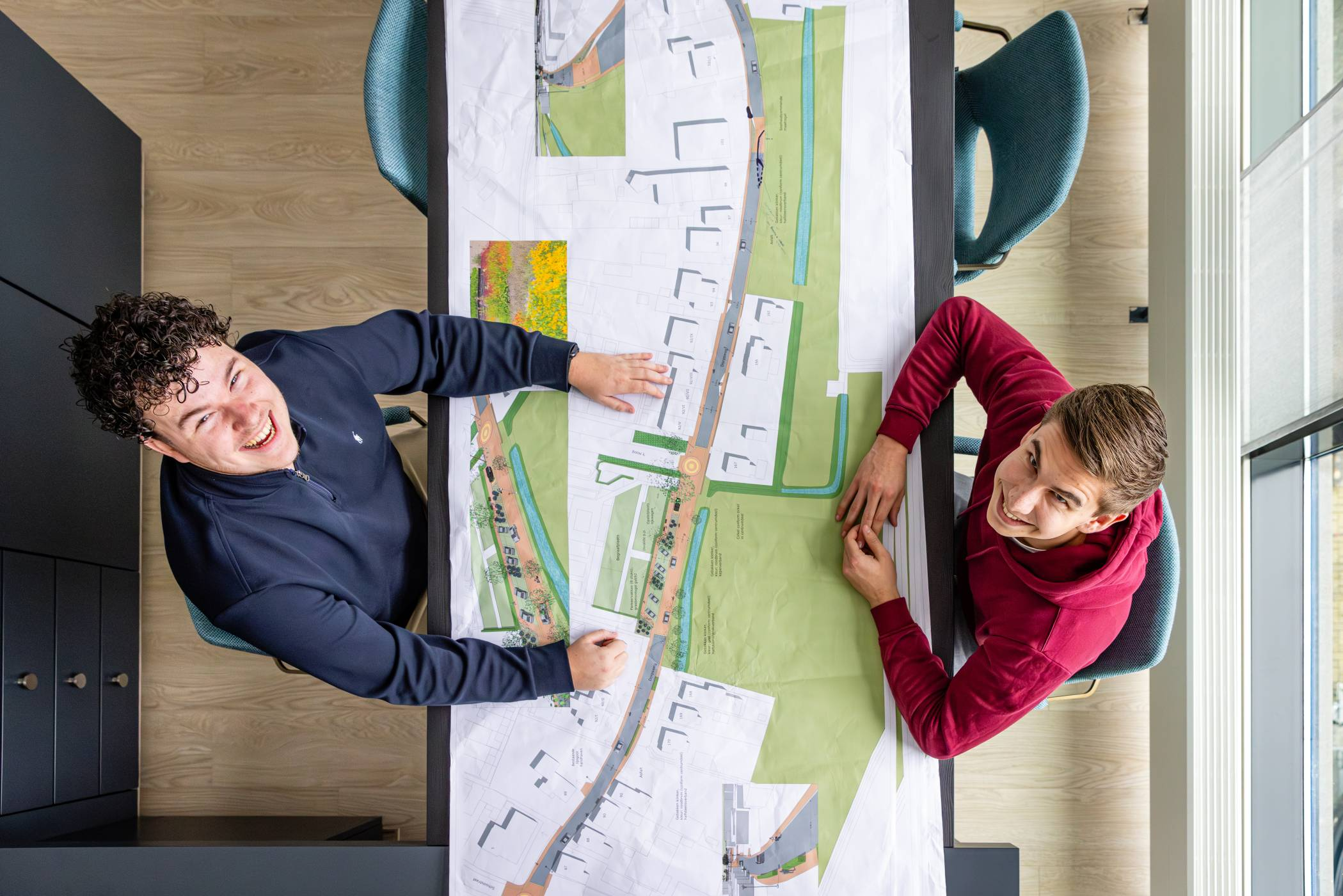 mannen overleggen aan een bureau met een kaart erop en kijken omhoog in de camera