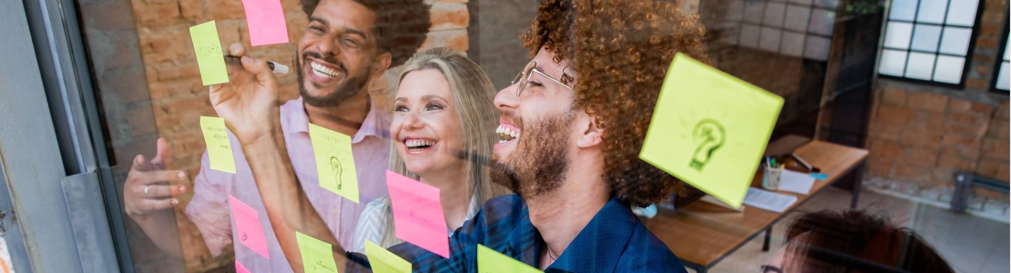 Groep jonge mensen plakken post-its op een glazen wand in een kantoor
