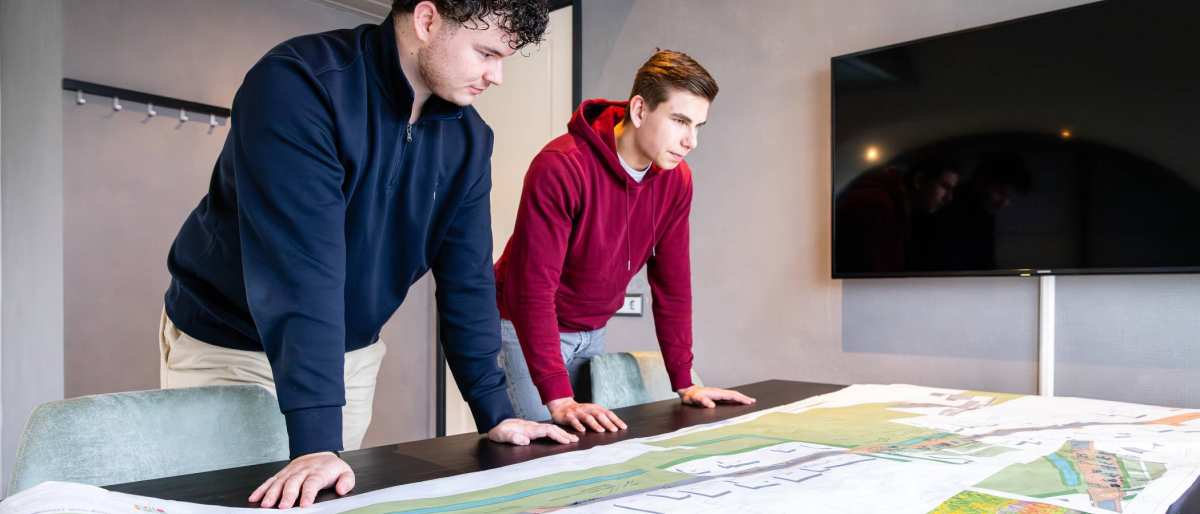 Twee mannen leunen op een bureau met daarop een omgevingskaart.