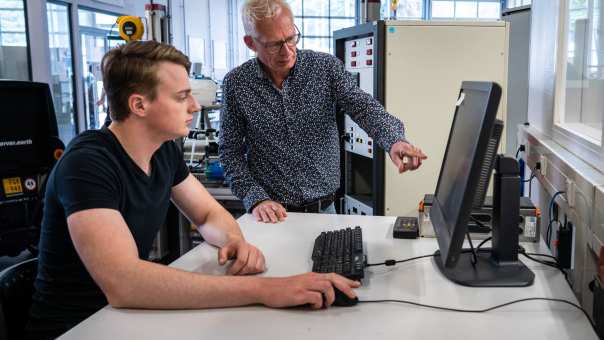 Docent Automotive wijst iets aan op het computerscherm van een student, bij de waterstoftafel.