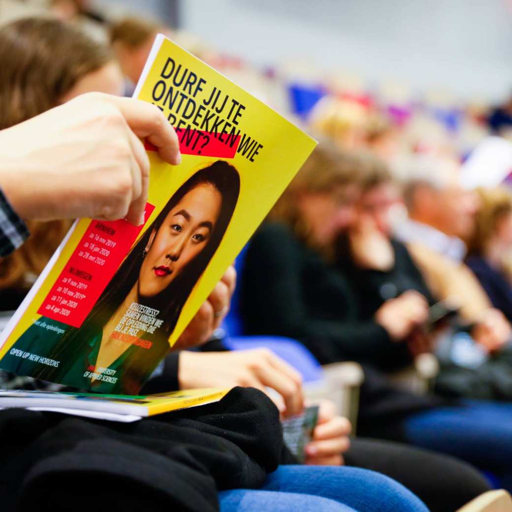 Bezoeker bladert door HAN magazine voltijd brochure in auditorium bezoekers op achtergrond