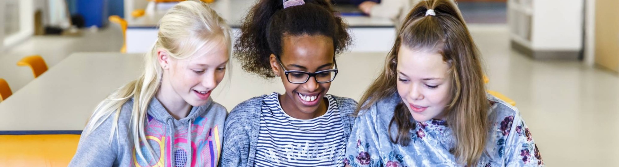 Drie kinderen zitten op een rijtje achter hun laptop met blauwe hoes.