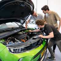 Studenten en docent automotive kijken naar de motor van de auto.