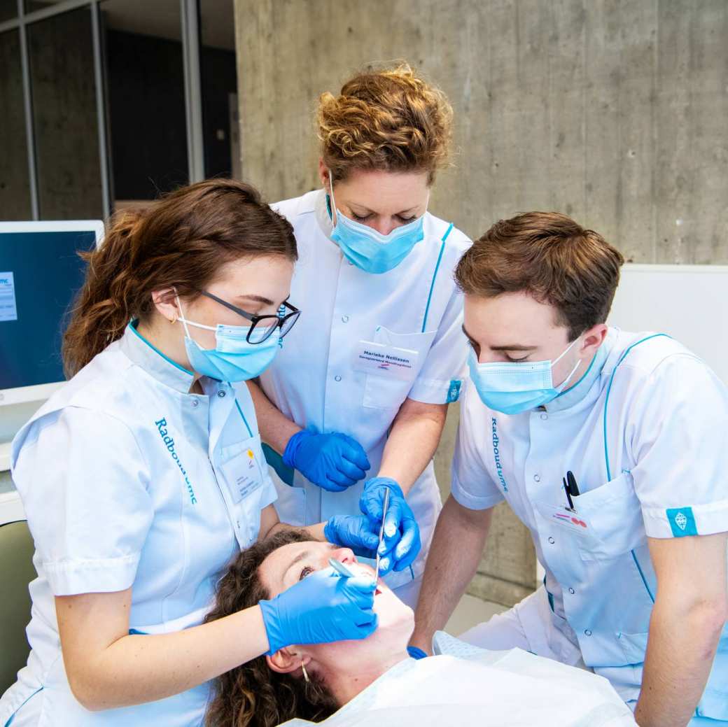 2 studenten en een docent kijken in de mond van een patient op een behandelstoel.