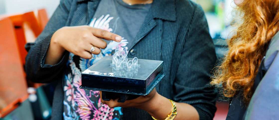 IPO-student Tayisha wijst een 3d geprint product aan student Elena in Fab Lab bij Industrieel Product Ontwerpen