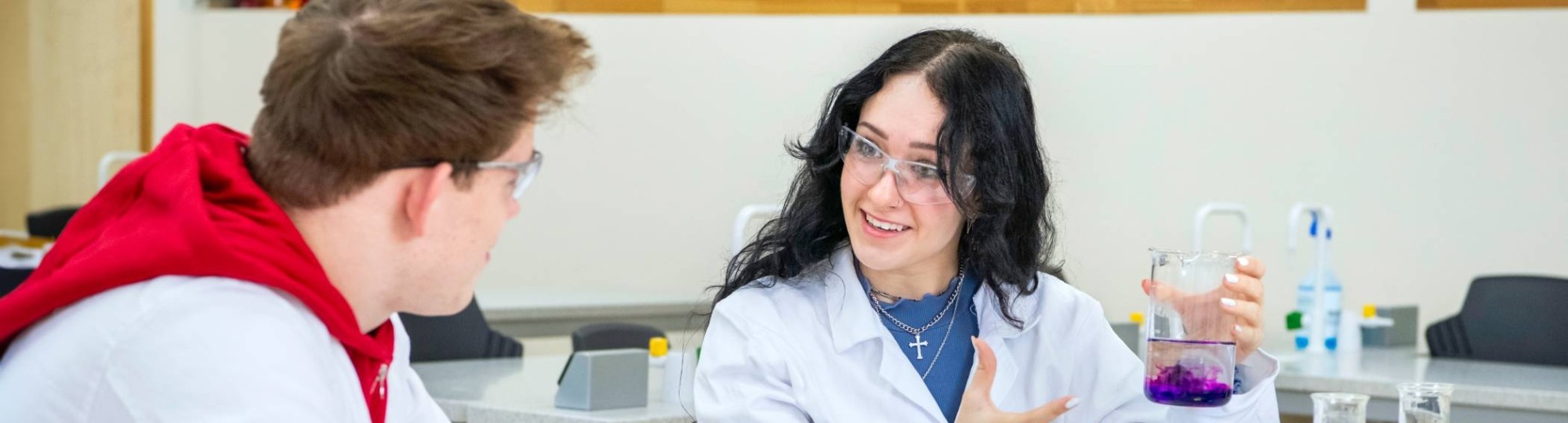 Twee studenten Leraar Scheikunde voeren een experiment uit en hebben een labjas aan en een veiligheidsbril op.