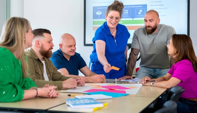 Een groep studenten van de opleiding Learning & Development in Organisations deeltijd. Ze werken samen met post-its en vellen.
