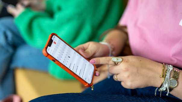 Student houdt haar telefoon vast en wijst er met haar vinger iets op aan. 