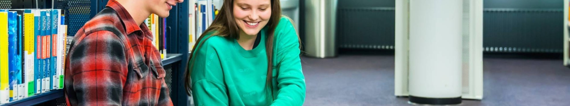 jongen en meisje studeren samen op de grond in studiecentrum en zij wijst iets aan