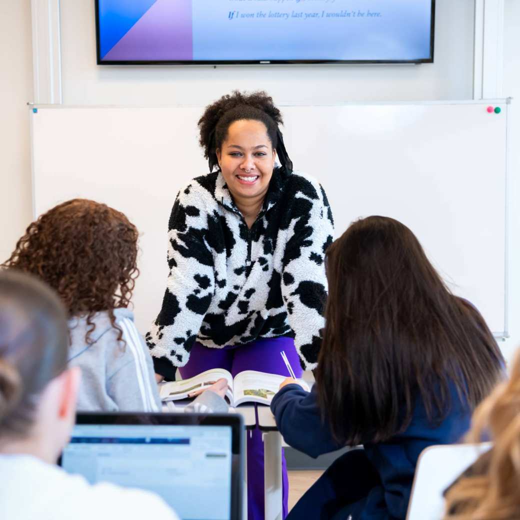 Docent luistert naar haar drie studenten die aan de tafel zitten te overleggen.