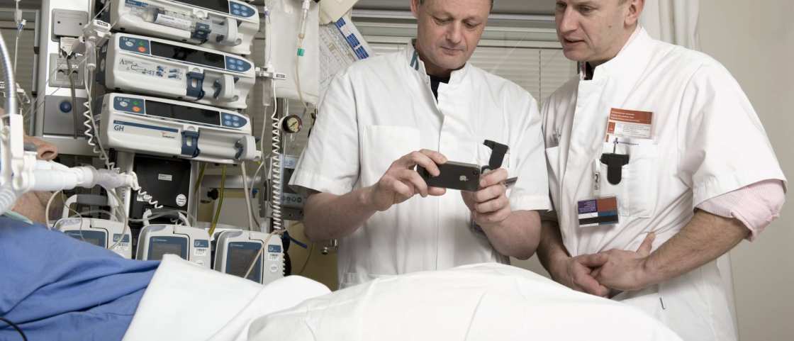 2 mannen verpleegkundigen bekijken app op mobieltje aan bed IC
