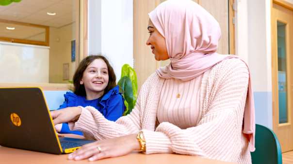 Juf legt iets uit aan een leerling en wijst naar de laptop