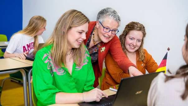 Lerarenopleider helpt twee studenten door iets aan te wijzen op de laptop die voor hun staat.
