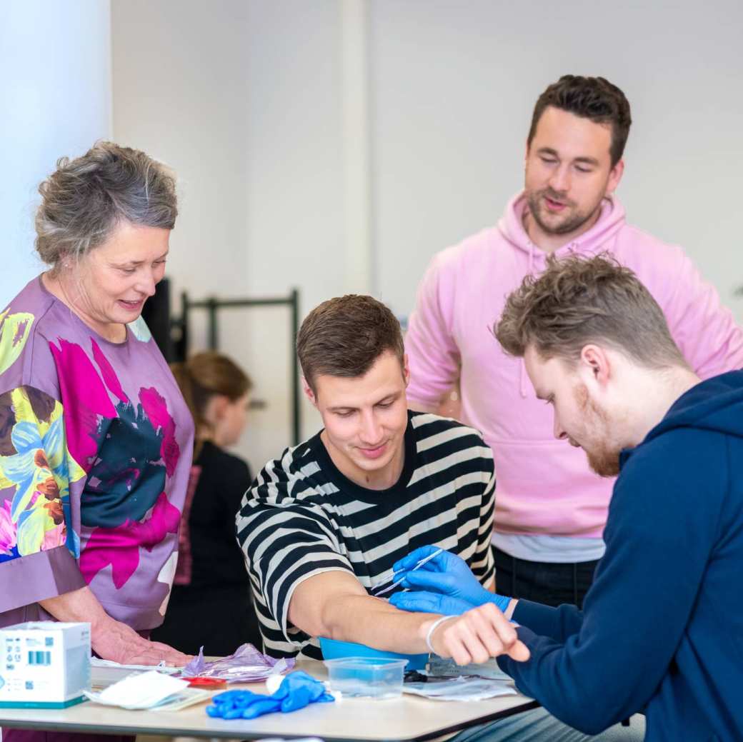 Docent kijkt mee met 3 studenten tijdens wondverzorging les Verpleegkunde deeltijd