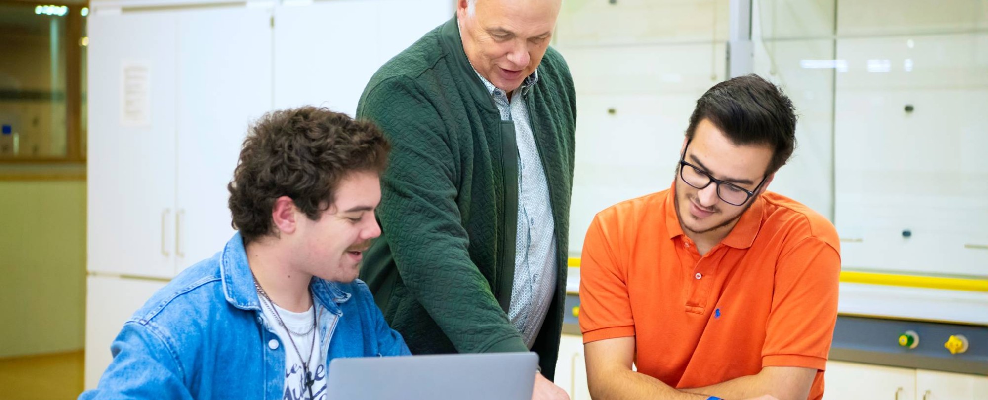 De leraar wijst twee studenten in een boekje wat aan.
